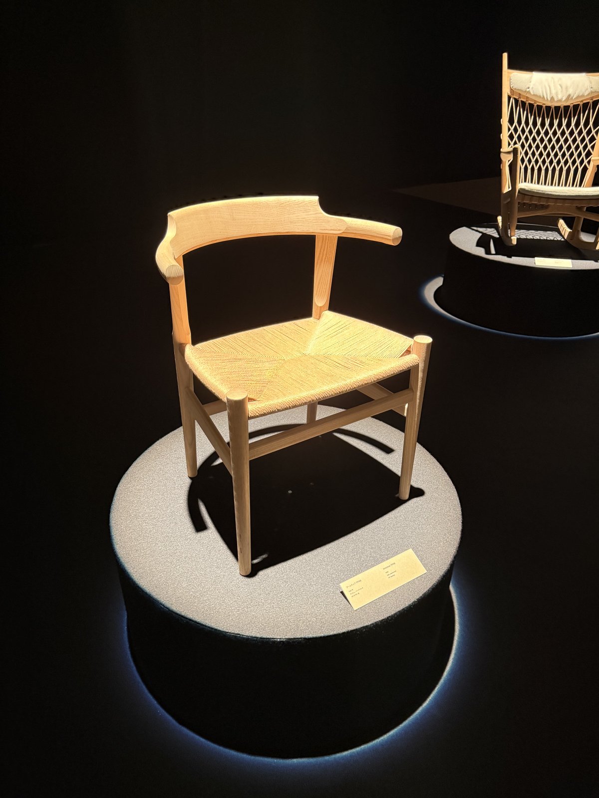 明るい木のフレームにペーパーコード座面の椅子と、奥にロッキングチェアらしき椅子が並ぶ展示の様子